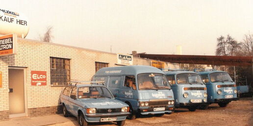 Historisches Firmengebäude mit mehreren blauen Firmenfahrzeugen, darunter Transporter und PKW, vor dem Firmensitz der Firma Borgmann.