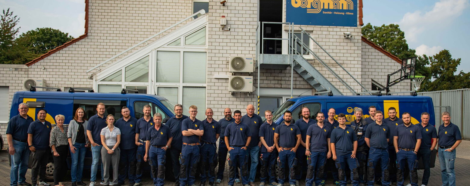 Gruppenfoto des gesamten Borgmann-Teams in Arbeitskleidung vor dem Firmengebäude mit zwei blauen Firmenfahrzeugen